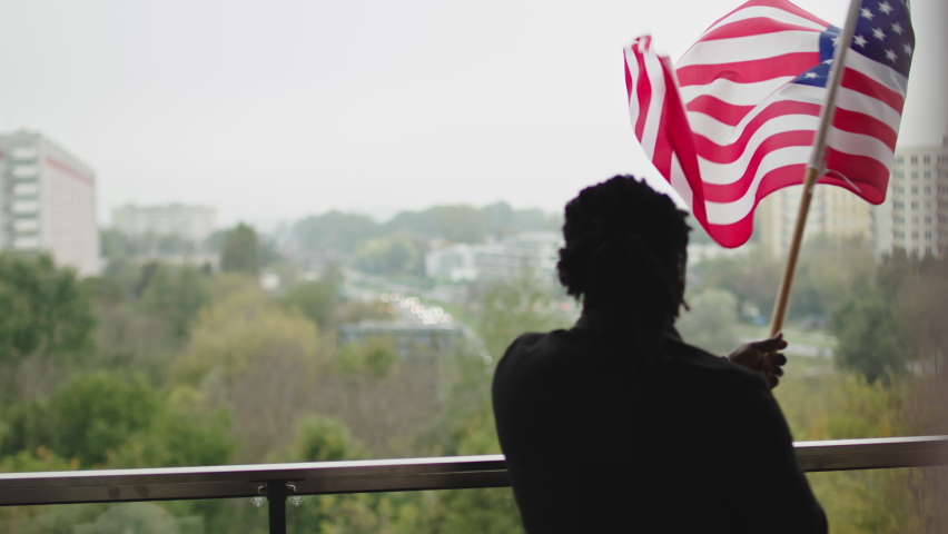 Patriotic black man waving American flag from the balcony. View from behind