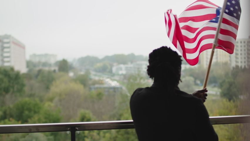 Patriotic black man waving American flag from the balcony. View from behind Royalty-Free Stock Footage #1061523088