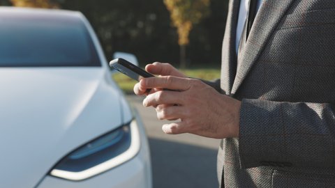 Businessman controls a self-driving electric car using mobile application. Autonomous autopilot driverless car. Smartphone app. Sensor scanning road ahead for vehicles, danger, speed limits