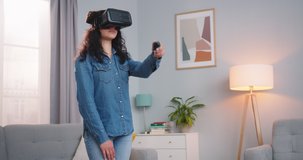 Good-looking Caucasian woman in virtual reality headset standing in living room. Pretty young lady using joystick to draw circle in air and looking at it. Technology, entertainment, vr concept.