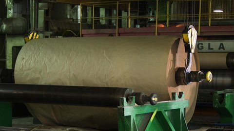 A production crane lifts a large roll of manufactured paper.