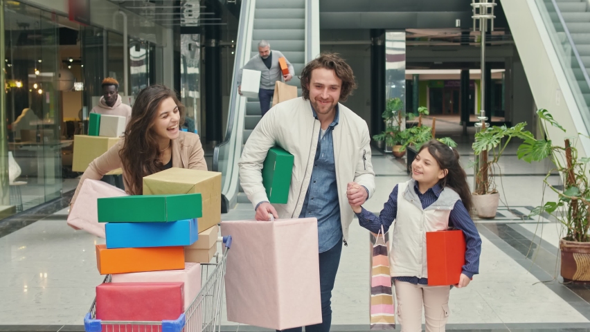 Family Spending Weekend in The Shopping Mall. Smiled Parents Walking Hand in Hand With a Daughter With Bags From Shop. Family Christmas Shopping.