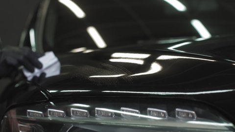 Car detailing - Man applies nano protective coating or wax on black car. Covering car bonnet with a liquid glass polish
