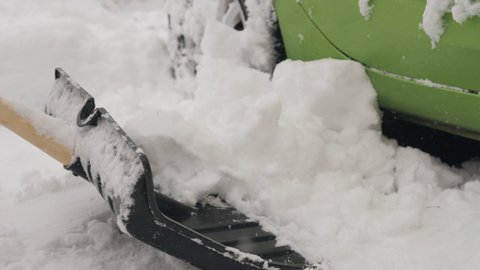 Close-up of a woman with a shovel-cleans snow near the wheels of the car in the back yard.