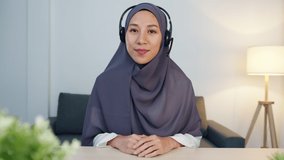 Asia muslim lady wear headphone using laptop talk to colleagues about sale report in conference video call while working from home office at night. Social distancing, quarantine for corona virus.