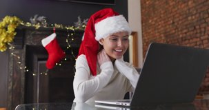 Caucasian woman at home at Christmas, wearing Santa hat, making video call on laptop, smiling and blowing a kiss, slow motion. Social distancing during Covid 19 Coronavirus quarantine lockdown.