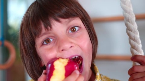 Сheerful teenager bites big apple. He looks into the camera with his eyes. A vegetarian can be a healthy choice for child. Healthy eating child.