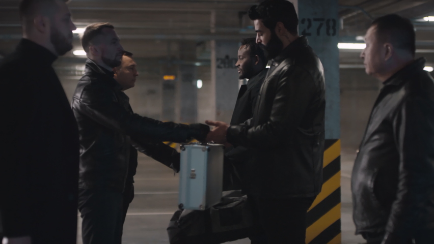 Medium footage of two criminal squads in leather jackets exchanging metal briefcase with money for prohibited bag contents at underground parking lot | Shutterstock HD Video #1061533399