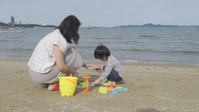 4K Video Mother and 3 years old asian kid play sand on the beach. Background for family life and education. holiday with children.