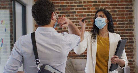 Mixed race female and Caucasian male business creatives, in modern office wearing face masks greeting touching elbows in slow motion. Health and hygiene in workplace during Coronavirus Covid 19 pande