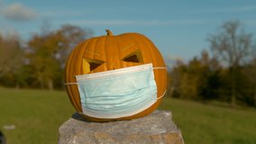 SLOW MOTION CLOSE UP: Halloween carved pumpkin with medical face mash gets smashed with baseball bat. Funny video of orange pumpkin wearing a Covid virus facemask and gets beaten up and destroyed
