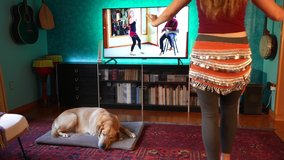 Woman follows workout fitness dance lesson online at home. Exercise watching personal trainer livestreaming on tv social media web channel.