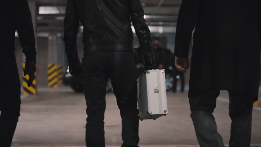 Tilting up footage of gangster leader with squad carrying metal briefcase walking to other multi ethnic mobsters ready for making deal at underground parking | Shutterstock HD Video #1061539564