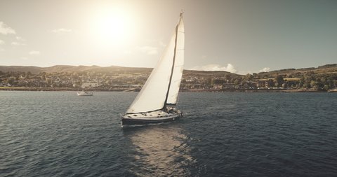 Racing yacht at sun reflection on sea bay aerial. Nobody nature seascape with sail boat at sunshine. Port town cityscape at green highland with mountain shore landscape. Cinematic drone shot