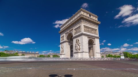 The Arc de Triomphe (Triumphal Arch of the Star) timelapse hyperlapse with traffic on circle road. Famous monument in Paris, standing at the western end of the Champs-Elyseees. Blue cloudy sky at