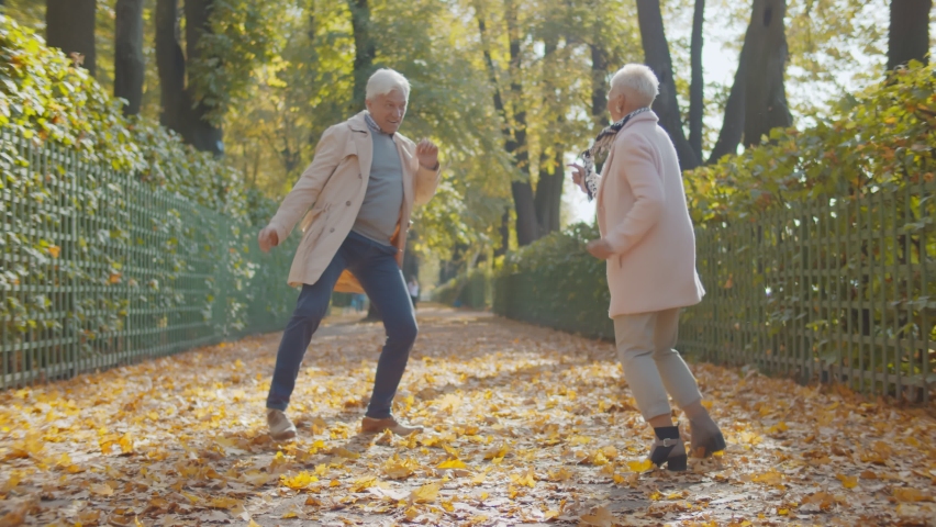 Happy beautiful senior couple dancing in autumn park. Full length portrait of cheerful active retired man and woman dancing and smiling in fall city park enjoying autumn vibes Royalty-Free Stock Footage #1061545699