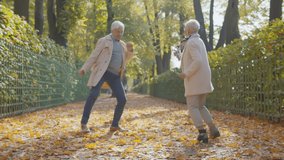 Happy beautiful senior couple dancing in autumn park. Full length portrait of cheerful active retired man and woman dancing and smiling in fall city park enjoying autumn vibes