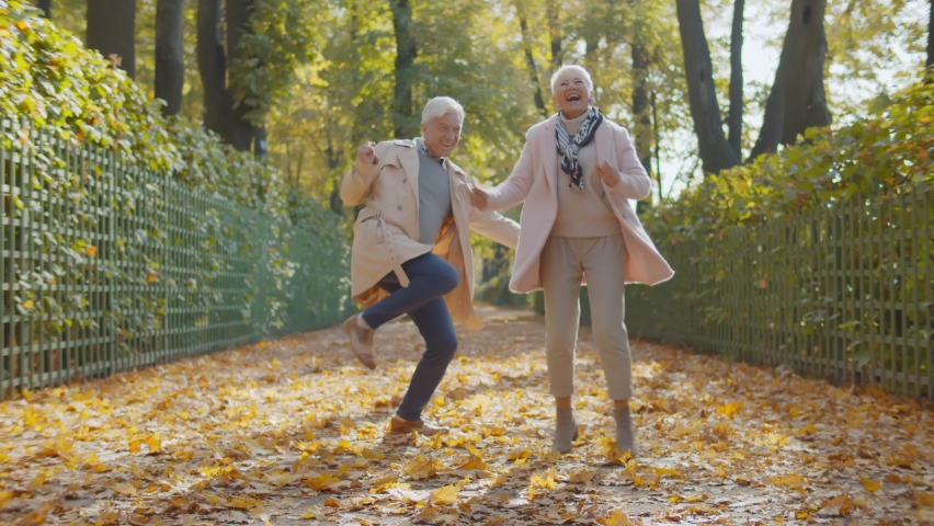 Happy beautiful senior couple dancing in autumn park. Full length portrait of cheerful active retired man and woman dancing and smiling in fall city park enjoying autumn vibes Royalty-Free Stock Footage #1061545699