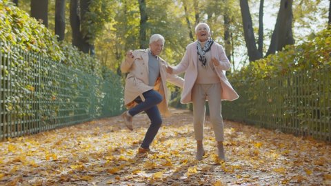 Happy beautiful senior couple dancing in autumn park. Full length portrait of cheerful active retired man and woman dancing and smiling in fall city park enjoying autumn vibes