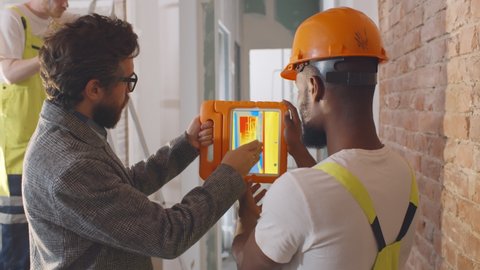 Back view of engineer and foreman analyzing thermal image of heat using thermal camera. House owner and worker using thermal scope app on tablet inspecting renovation process