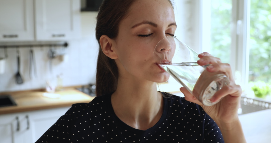 Close up head shot thirsty young 20s european girl drinking pure stilled aqua in kitchen, feeling energetic in morning, beautiful woman hydrating organism with fresh water, enjoying healthcare routine | Shutterstock HD Video #1061547394