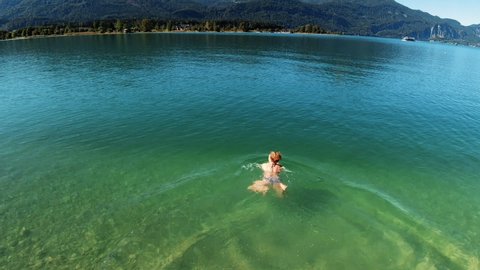 A woman plunges into the beautifully clear alpine lake Wolfgangsee and swims. A beautiful sunny day in the mountains. Alps, Austria - 05.12.2019