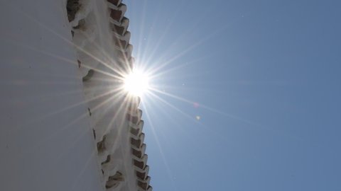 Sun in blue sky passing a line of tiles on an Andalusian roof at noon
