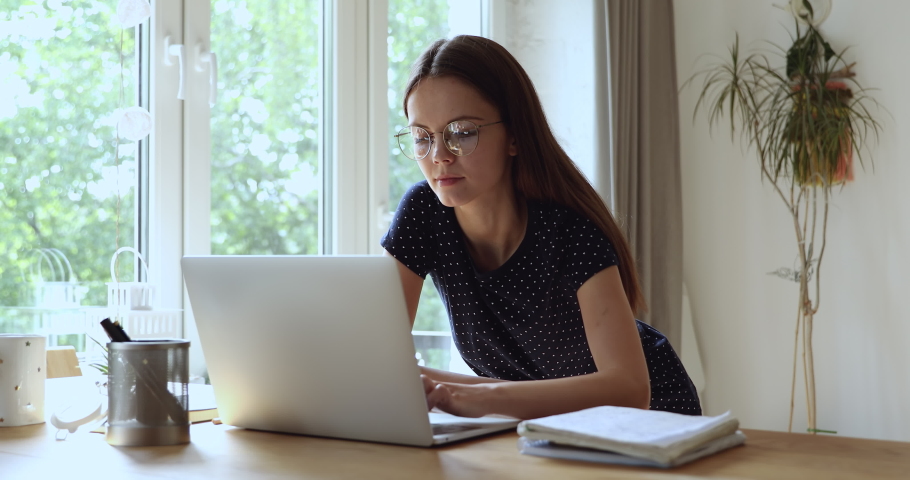 Happy young european appearance beautiful woman in eyeglasses studying on computer, enjoying communicating with friends in social networks, smiling female freelancer working on laptop at home office. Royalty-Free Stock Footage #1061553160