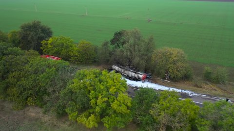 Top aerial view of the fuel truck crashed into a tree and caught fire. Fire truck and ambulance came to the rescue. Accident on the road. 