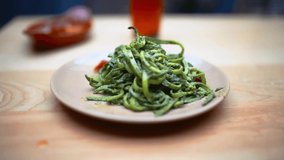 4K slow-motion video of a hand spinning a fork in a zucchini noodles dish on a wooden table with a blurry plate and bottle as background