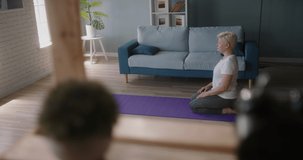 Mature caucasian woman is exercising at home, watching an online video on her laptop and stretching - wellness, heathy lifestyle concept top view 4k footage