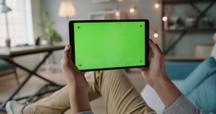 Caucasian guy having an online video conference, using tablet with mockup green screen, doing distant learning during self-isolation 4k footage