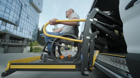 A man who uses a wheelchair on a lift of a vehicle for people with disabilities. Lifting equipment for people with disabilities - man in wheelchair near the vehicle