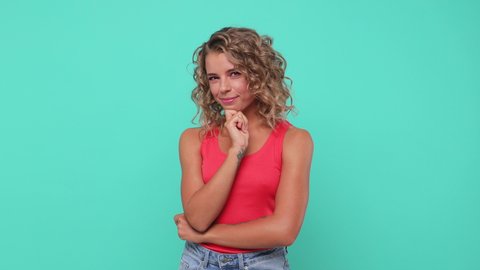 Smiling pretty pensive blonde young woman 20s years old in pink tank top posing isolated on blue turquoise colour background studio. People lifestyle concept. Looking aside up put hand prop up on chin