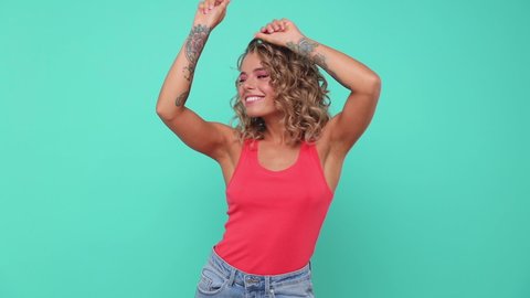 Smiling cheerful funny blonde young woman 20s years old in pink tank top posing isolated on blue turquoise colour background in studio. People lifestyle concept. Looking camera dancing waving hands