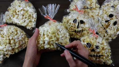 Process of making goodies for Halloween party, Woman drawing a skull on the plastic bag with popcorn