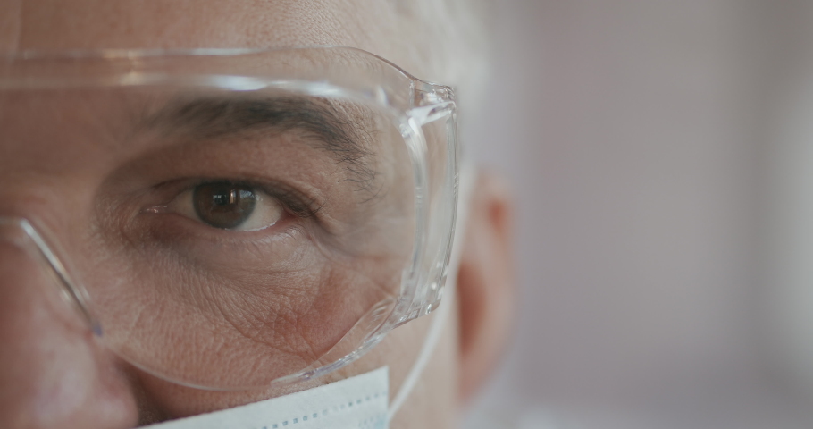 Male doctor or nurse in uniform, mask and glasses looking straight at camera. Close up of eye. slow motion | Shutterstock HD Video #1061571514