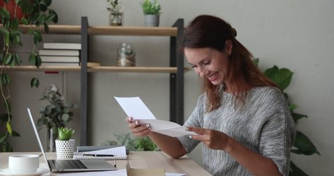 Happy young woman opening paper correspondence letter, reading good news, satisfied with bank loan approval or excited by interesting event invitation, celebrate professional achievement success.