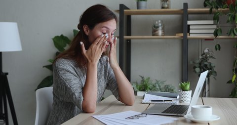 Stressed young businesswoman taking off glasses, feeling tired due to computer overwork, massaging nose bridge, exhausted female entrepreneur workaholic suffering from blurry vision at home office.