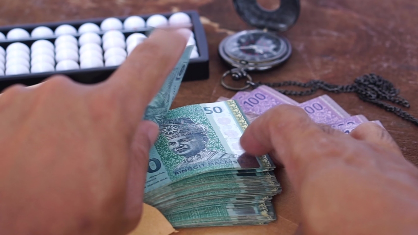 The hand is counting fifty Ringgit Malaysia banknotes with a vague abacus background | Shutterstock HD Video #1061575774