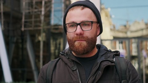 Portrait of bearded guy looking gloomy and disappointed while walking at city street. Close up view of worried sad man in glasses lost his job or having bad news. Concept of emotions