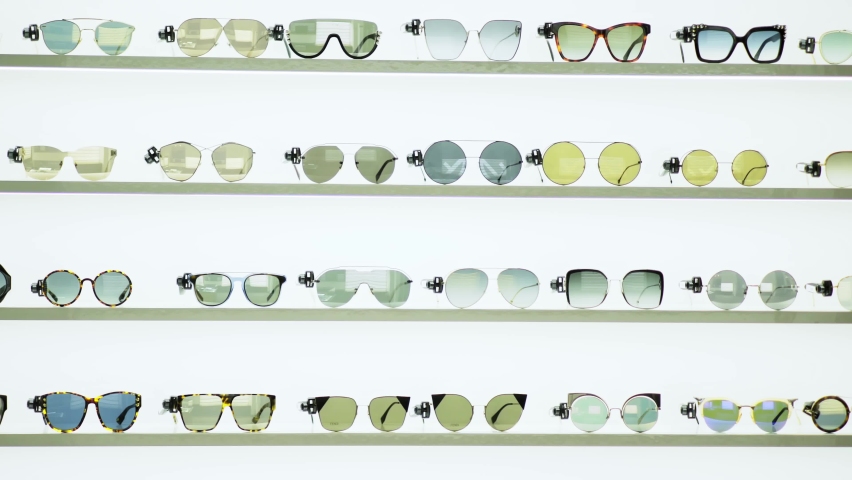 fashion boutique stand panorama motion shot on various modern designer sunglasses lying on shelves in white background closeup