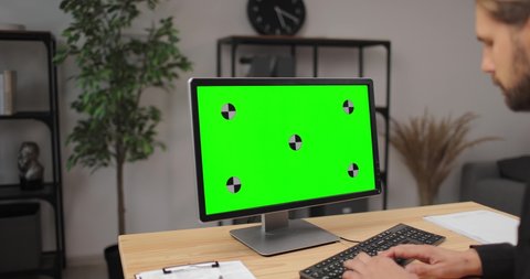 Handsome office worker in business suit using modern computer at bright office. Empty green screen. Space for text and advertisement.