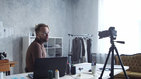 Young fashion blogger is recording video blog about design of clothes. Stream of talented stylist from his workplace in modern loft.
