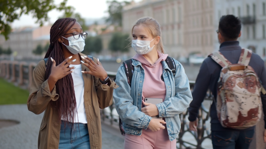 Multinational student women in medical mask talking while walking down city street. African and caucasian young female in safety mask strolling in city and chatting Royalty-Free Stock Footage #1061585536