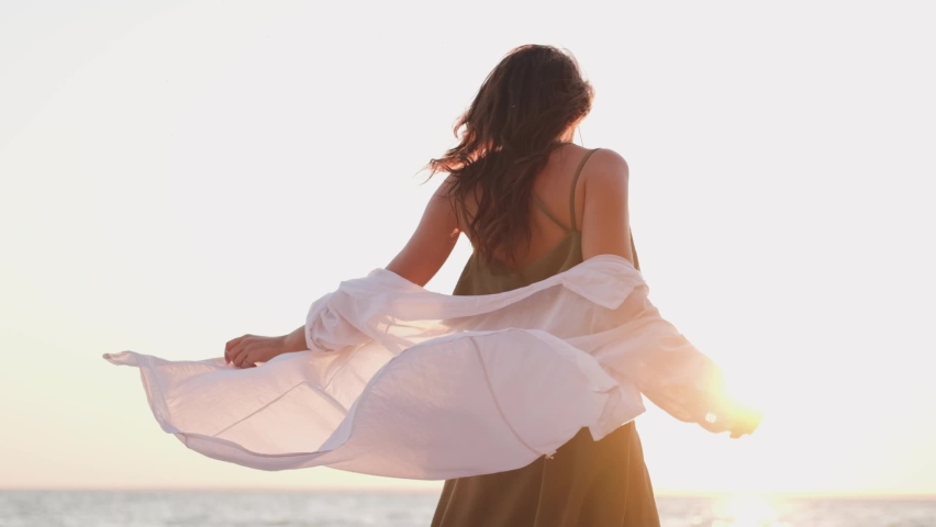 beautiful girl dancing on the beach in a white shirt. Free girl with long hair in a white shirt dances in the sunset. Healthy woman dancing on the beach. Royalty-Free Stock Footage #1061587561