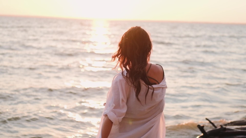 beautiful girl dancing on the beach in a white shirt. Free girl with long hair in a white shirt dances in the sunset. Healthy woman dancing on the beach. Royalty-Free Stock Footage #1061587570