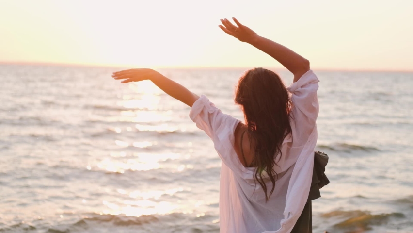 beautiful girl dancing on the beach in a white shirt. Free girl with long hair in a white shirt dances in the sunset. Healthy woman dancing on the beach.