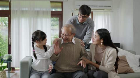 Asian elderly senior male grandpa sitting at sofa couch at home living room on quarantine in concept healthcare, chronic health issue or low back pain in retired older people with family.