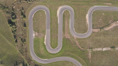 Wide aerial view of a person riding a motorcycle in a closed racing track. Top view of a curved racing track. Aerial footage of a curved racing road.